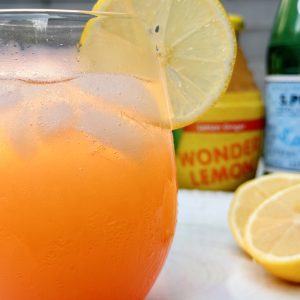 Orange lemon drink with ice, lemon slices, and a Wonder Lemon bottle behind it.