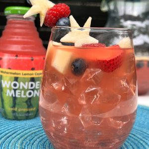 Pink fruit drink with berries and star-shaped fruit beside a Wonder Melon bottle.