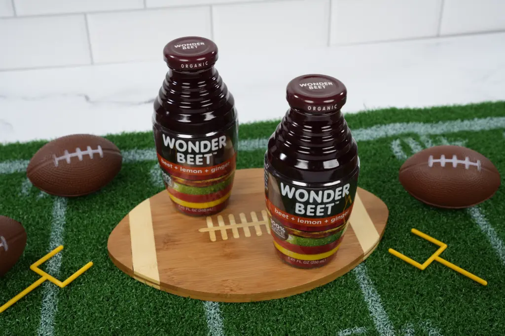 Wonder Beet bottles placed on a wooden football plate on a football field mat, with footballs and yard lines in the background.